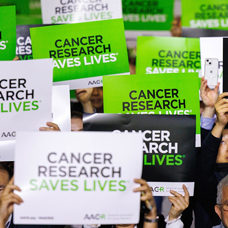 Attendees holding up “Cancer Research Saves Lives” signs at the AACR Annual Meeting 2025